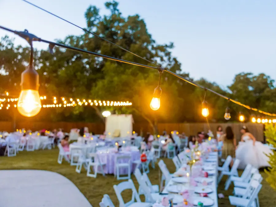 An outdoor wedding reception at sunset, guests seated under string lights